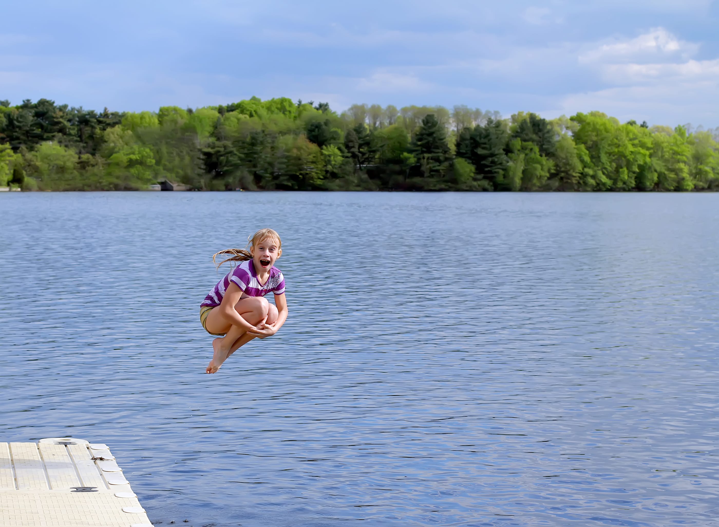 Girl doing a cannonball off a dock into a lake